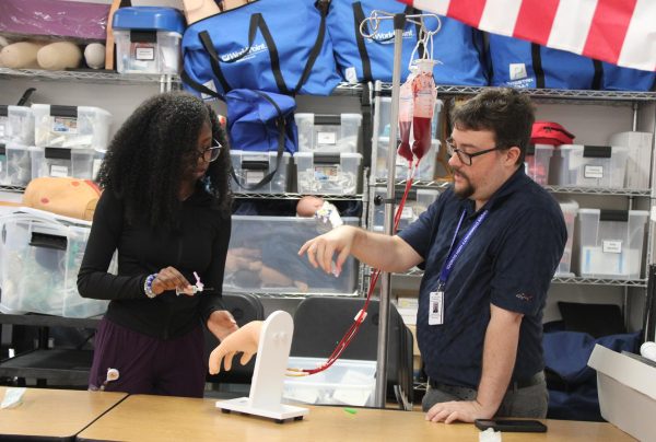 IV INSERTION: Medical teacher Mr. Hartung instructing junior LPN, Midwina Alcema, on how to place an intravenous line.