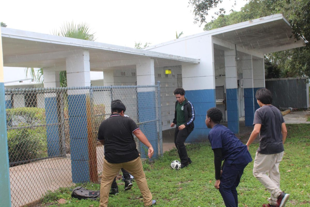 LET US PLAY: Despite the rain, a group of students continued to play a game of soccer outside of building 4.